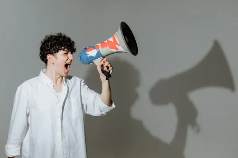 Young adult with curly hair energetically shouting through a colorful megaphone.